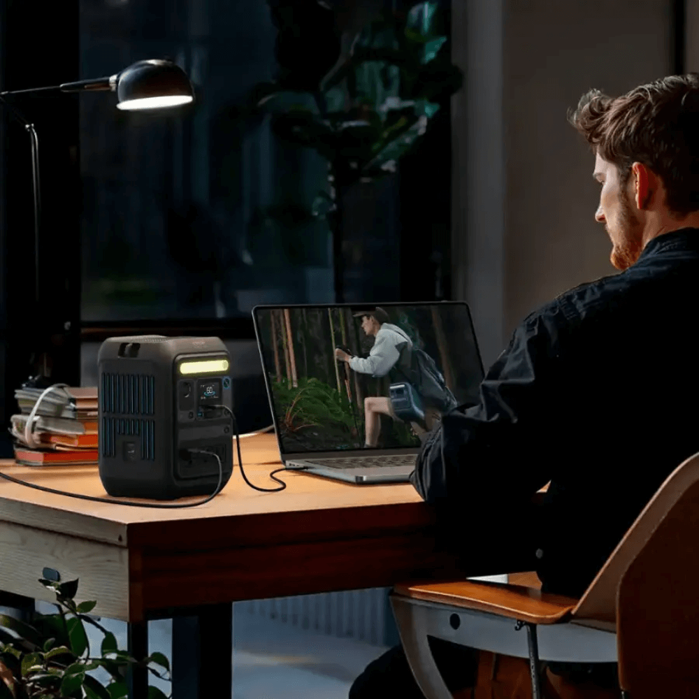 Man using Anker SOLIX C300X Portable Power Station while working at a desk with a laptop in a cozy indoor setting.